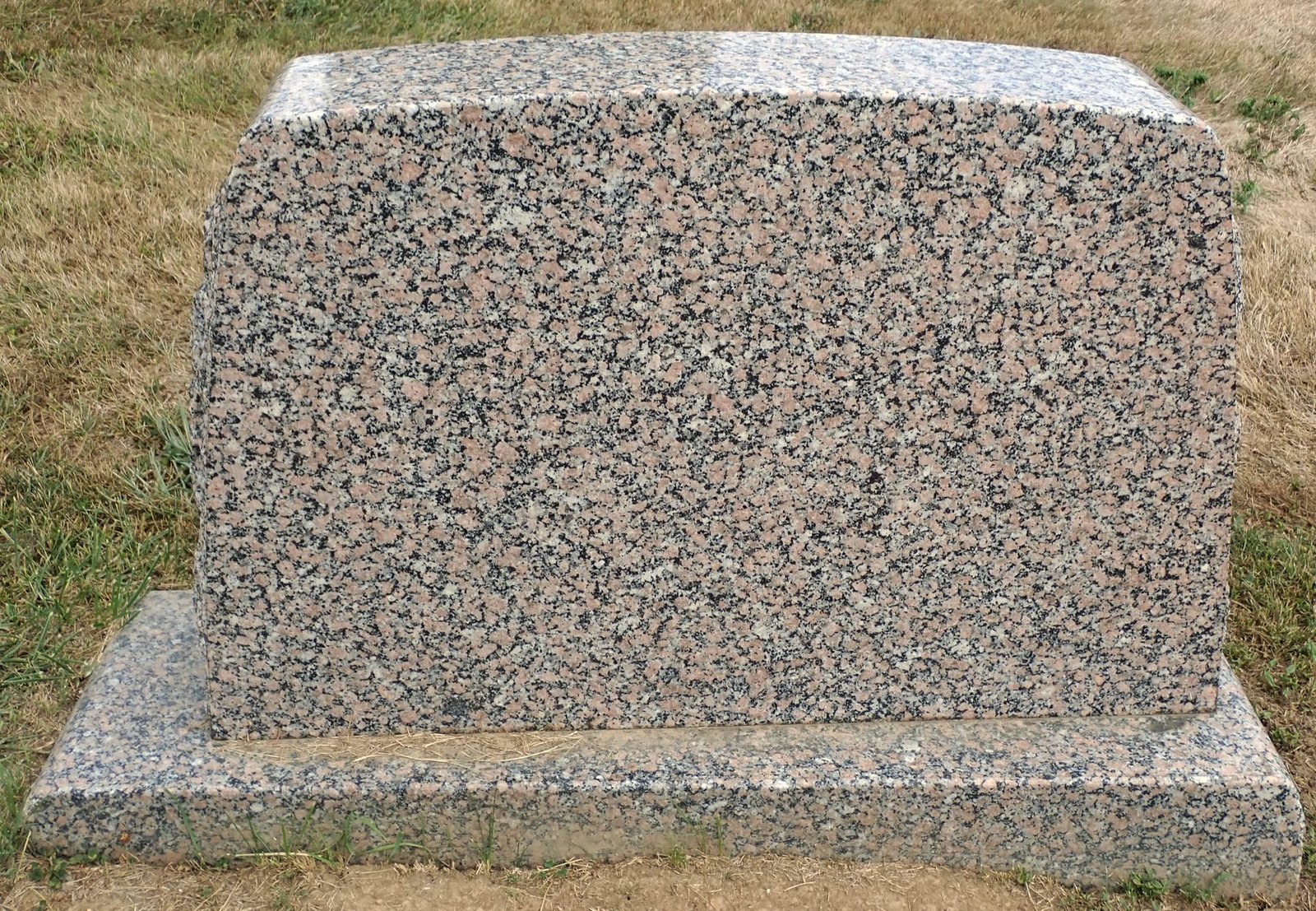 A blank upright headstone of speckled pink granite on a rough-cut base