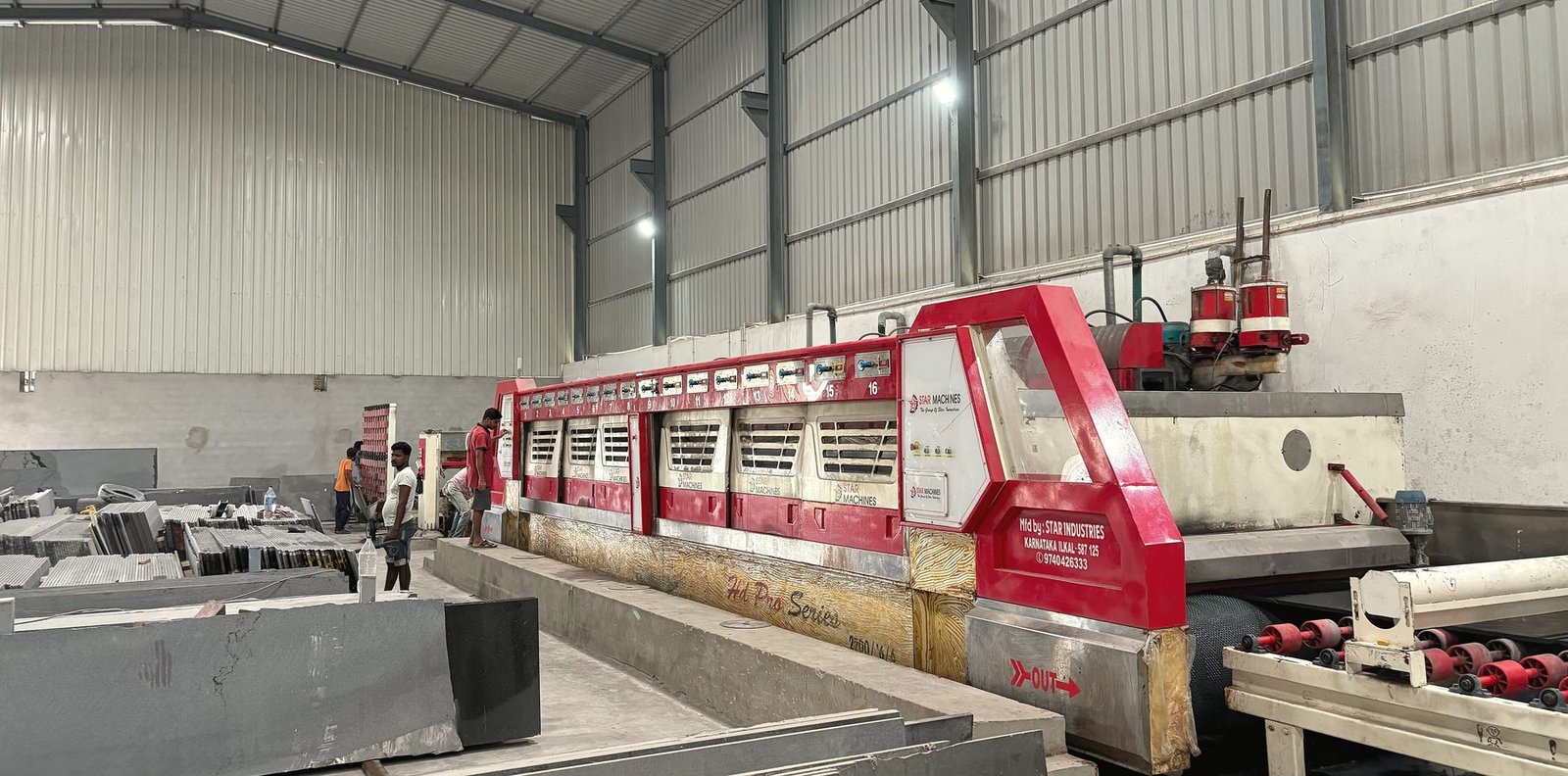 A long red polishing machine running over grey slabs inside a steel shed