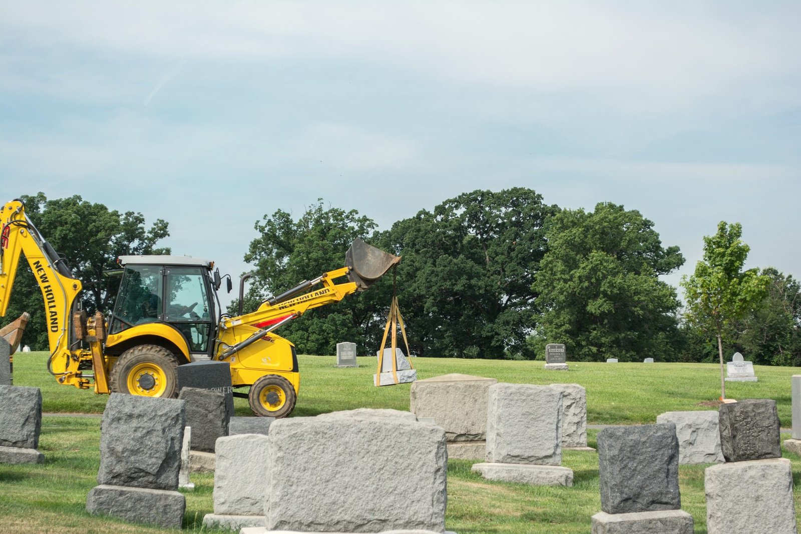 A backhoe in a cemetery beside rows of new granite stones