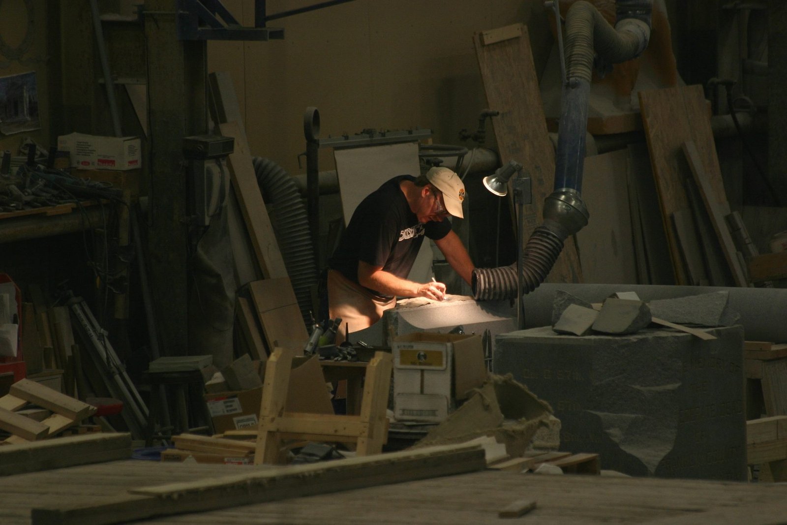 A worker bent over a lit bench, finishing a piece of dark granite
