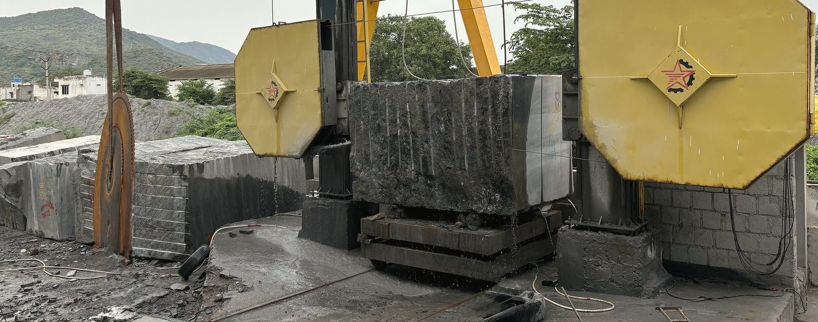 A granite block sitting between the two yellow wheels of a wire saw